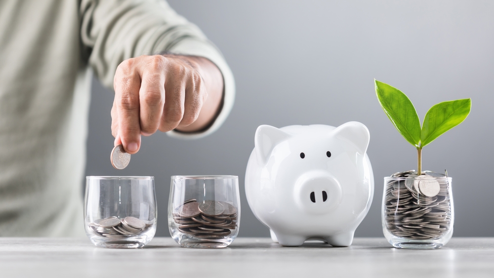 Man putting coins in savings jars with piggy bank